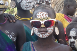 „Da’s nun ernst wurde mit dem Gruppenphoto, setzte sich Trattner die Sonnenbrille auf, so fiel’s ihm leichter. Sofort wollten ein paar Jungen die Brille haben, im Getümmel wäre er fast umgerissen worden. Einer der Jungen zerrte so zudringlich an ihm, bis ihm Trattner die Brille überließ. Sie war viel zu groß für sein Gesicht, eine weiße Sportbrille mit orangerot verspiegelten Gläsern, die schon oft für Aufsehen gesorgt und Trattner einigen Respekt eingebracht hatte. Die Brille ging von Junge zu Junge, erst spät trauten sich auch die Mädchen.“
