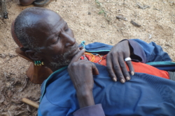 „Einige Männer lagen im Schatten, verstreut im sandigen Flußbett, das der Fluß während der Trockenzeit hier nur zur Hälfte einnahm. Alle Männer trugen aufwendig gepflegte Frisuren, wenngleich nur ein einziger eine Tonhaube. Die Köpfe hatten sie auf ihre kleinen Schemel gelegt, einige der Älteren schliefen mit aufgeknöpftem Hemd, weil sie ihre Brustnarben zeigen wollten. Der mit der Tonhaube hatte auffällig lange Fingernägel, oval gefeilt; aufgrund der dezent hindurchschimmernden Schmutzränder wirkte er trotzdem echt.“