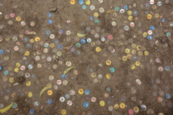 „In der Kneipe hatten sich erst einige Männer und Frauen eingefunden. Die meisten von ihnen schliefen, ausgestreckt auf dem Boden, aber da’s noch hell war und genügend Licht hereinfiel, konnte Trattner ohne Mühe darübersteigen. Das Bedele Beer lag, ein kleiner Haufen, in einem Eck, sie nahmen zwei Flaschen mit auf die Terrasse. Wie selbstverständlich setzten sie sich auf die Bank, die direkt an der Brüstung stand, dort waren schon einige Kronkorken in die Erde getreten, jetzt kamen zwei neue dazu.“