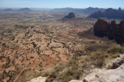 „Indem er so saß, gewöhnte er sich an die Weite der Ebene, die sich unter seinen Blicken in zart roten, braunen, beigen Tönen ganz langsam entrollte und bald endgültig liegenblieb, von grünen Linien durchzogen, wo während der Regenzeit Bäche verliefen. Er sah auf die Wege, die weiß getünchten Gehöfte, sogar die einzelnen Felder waren zu erkennen, terrassenartig aneinandergefügt, ein jedes anders gekrümmt und alle gleichermaßen ausgedörrt, nackte Erde in verschiednen Sonnenbrandtönen, ein Panorama von alttestamentarischer Strenge.“